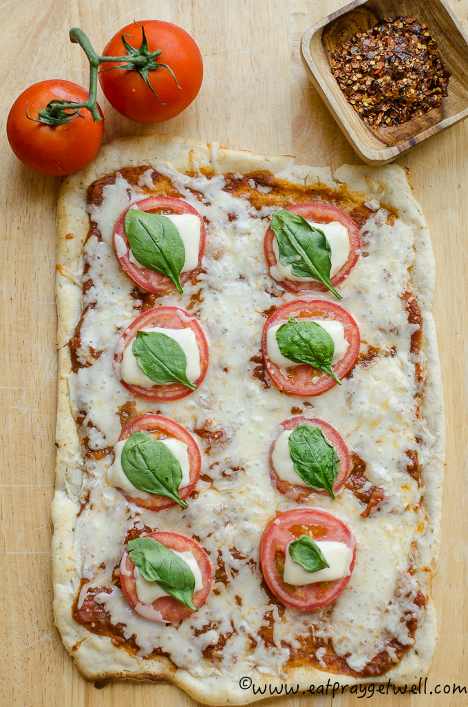 margarita pizza on a wooden table surrounded by tomatoes