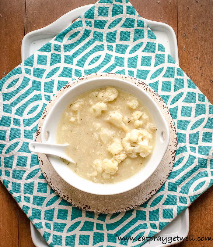 Cauliflower soup in a white bowl on top of decorative napkin