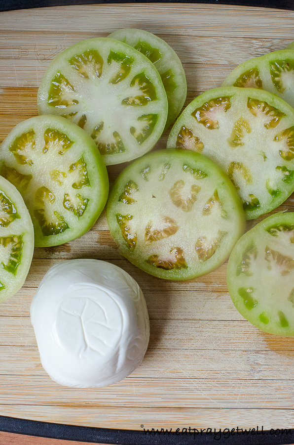 close up of green tomatoes on a cutting board with a ball of mozzarella cheese
