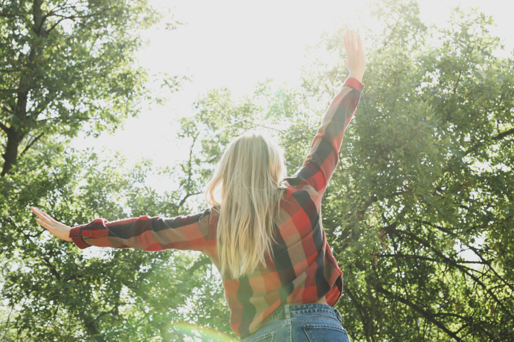Happy woman in shirt and jeans with raised arms outdoor